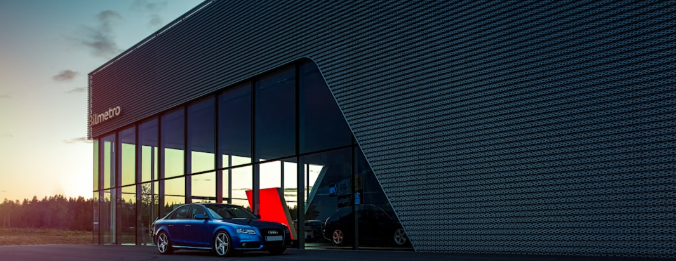 Modré Audi zaparkované pred moderným autosalónom Bilmetro počas súmraku.