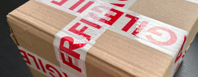 Detail kartónovej krabice prelepenej bezpečnostnou páskou s nápisom „FRAGILE“.