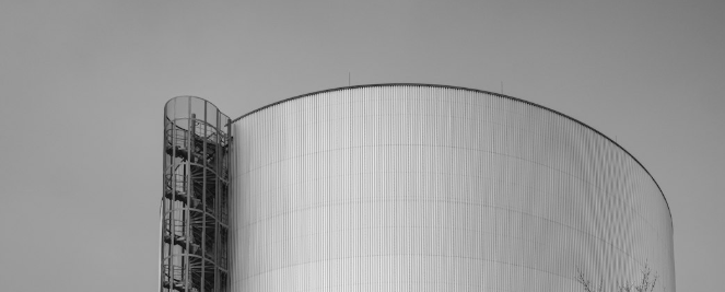 Čiernobiela fotografia veľkej priemyselnej nádrže s vonkajším točitým schodiskom.